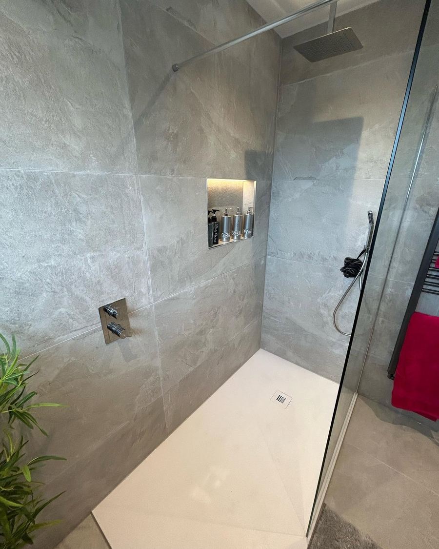 Walk-in shower in grey large-format tiles with a lit niche and wall-mounted valve.